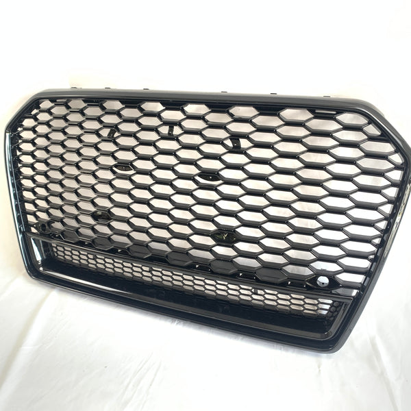 A hexagonal-patterned car grille, featuring a glossy black finish, rests on a white surface. The grille's design includes a prominent honeycomb structure, commonly used for automotive front ends.