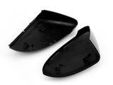 Two black plastic side mirror covers lie open, showing clips for attachment. They are positioned against a plain white background, highlighting their shape and design features.