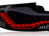 A car taillight with a sleek black design emits red light, featuring multiple illuminated segments. Blue label reads 