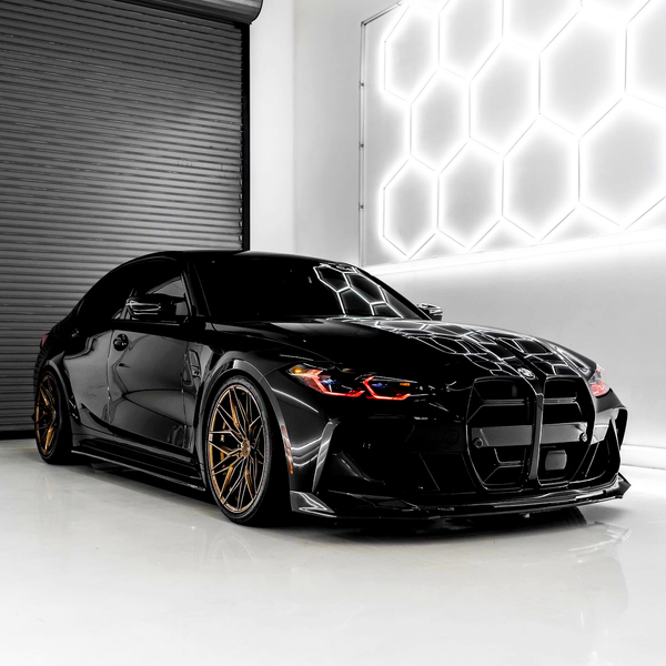 A sleek black sports car with bronze wheels is parked in a modern garage, reflecting hexagonal white lights from the wall, contrasting with a dark roller door.