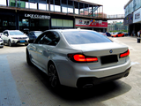 A silver BMW sedan is parked in a bustling urban setting, surrounded by other cars near buildings. Signs read 