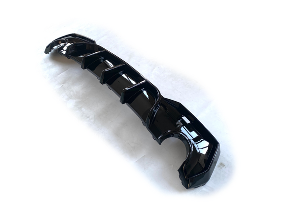 A glossy black car component, likely a diffuser, lies on a plain white surface. It features multiple aerodynamic fins and curves strategically positioned along its length.