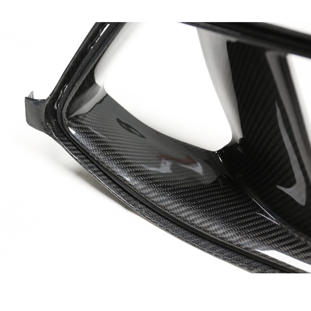 Carbon fiber auto part with a sleek, glossy finish, showing intricate patterning. The part is viewed close-up in a neutral setting, emphasizing its texture and craftsmanship.