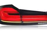 A sleek taillight, glowing red, features horizontal light bars and an amber strip along the bottom, set against a reflective white background. No text present.