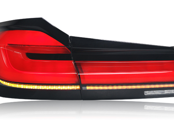 A sleek taillight, glowing red, features horizontal light bars and an amber strip along the bottom, set against a reflective white background. No text present.