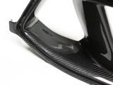 A carbon fiber car part resting on a white surface, displaying a glossy, textured finish with sharp edges and curves.