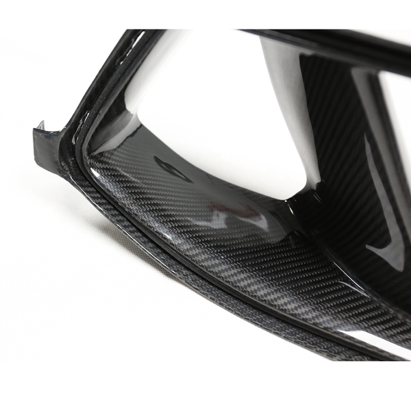 A carbon fiber car part resting on a white surface, displaying a glossy, textured finish with sharp edges and curves.