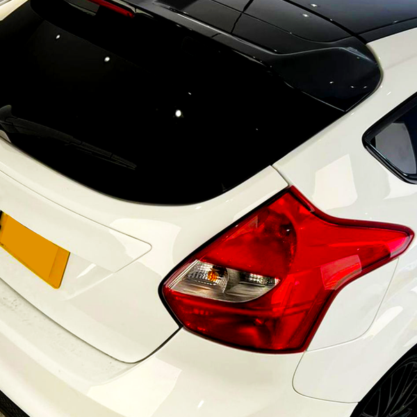 A white hatchback car is parked indoors, featuring red tail lights and a black roof. The setting includes a well-lit, modern interior space, with walls and floors visible.