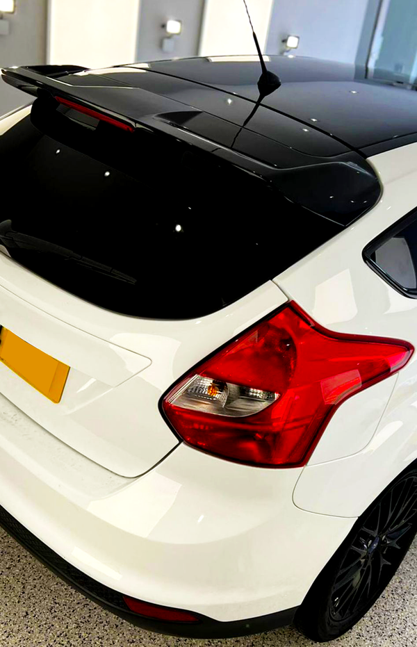 A white hatchback car is parked indoors, featuring red tail lights and a black roof. The setting includes a well-lit, modern interior space, with walls and floors visible.