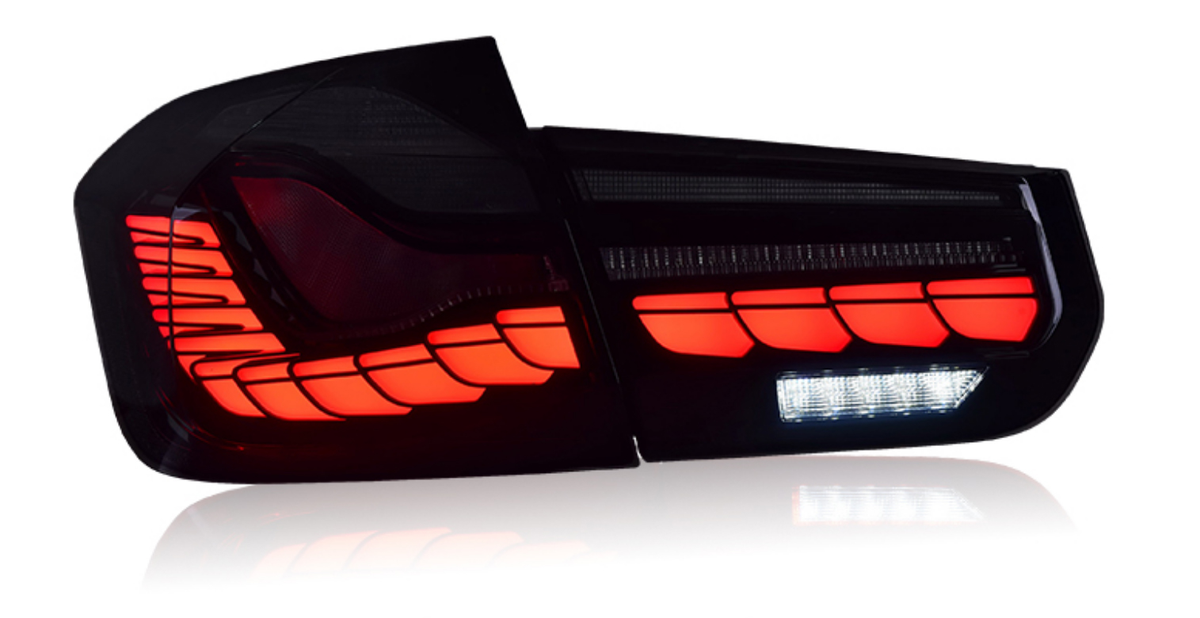 A car taillight glows with vibrant red LED segments, accented by a horizontal strip of white LEDs, set against a dark background, reflecting on a shiny surface.