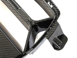Carbon fiber car grille, angular with a glossy finish, resting against a plain white background, showing intricate weave patterns and structural design details.