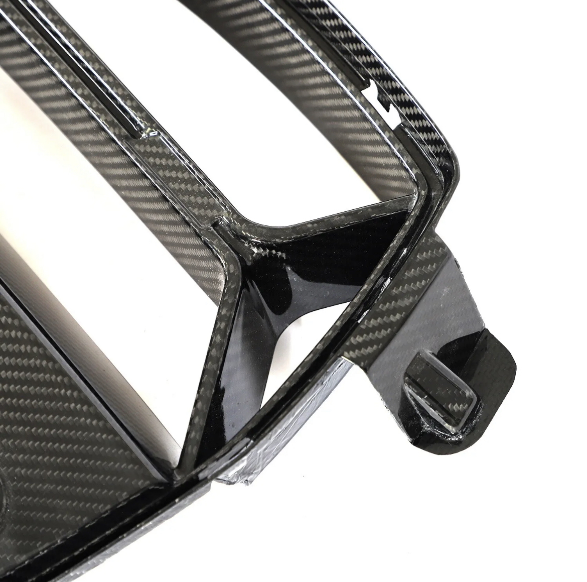 Carbon fiber car grille, angular with a glossy finish, resting against a plain white background, showing intricate weave patterns and structural design details.