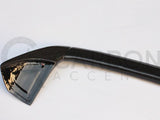 A black carbon fiber car spoiler rests on a white surface. Faint text in the background reads 