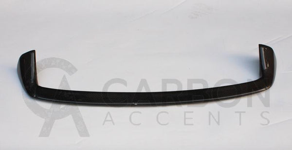 A carbon fiber car spoiler, curved and glossy, rests on a plain white surface. Text reads: "CARBON ACCENTS" with a partially visible stylized letter "A" behind the text.