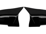 Two glossy black side mirror covers lie adjacent, separated, facing each other against a plain white background.