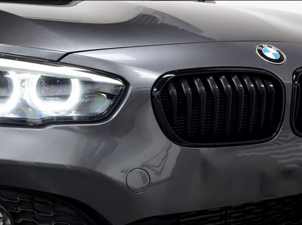 A car's front features illuminated headlights and a black kidney grille, with a BMW emblem on the hood, set in a glossy, grey exterior.