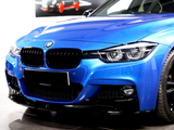 A blue BMW car is parked indoors, showcasing its sleek front grille, chrome logo, and shiny black wheels. The background features a blurred image of a car poster.