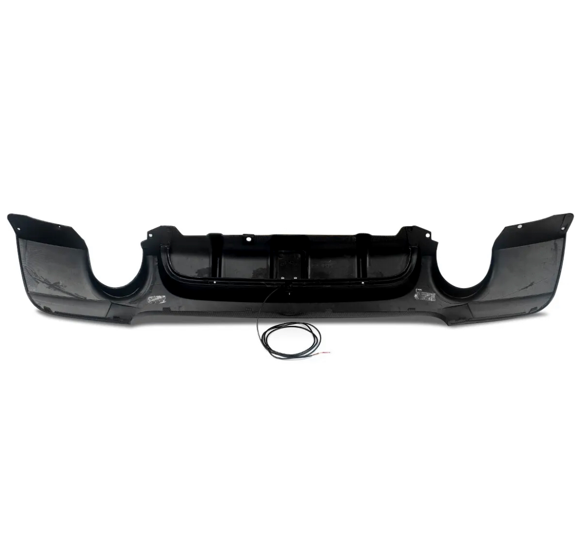 Black car bumper with aerodynamic design lying on a white background. A circular cable with exposed ends rests in front of the bumper.