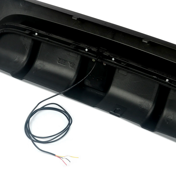Black bumper with visible wiring extending from it, placed on a smooth white surface, partially covered by a coiled black cable with exposed colored wires.