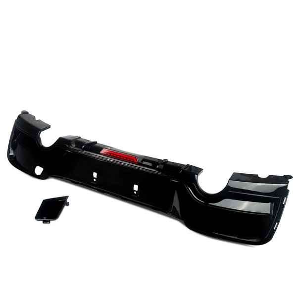 A black car bumper with integrated red reflector lies against a plain white background. A separate smaller black panel is positioned beside it, suggesting assembly components.