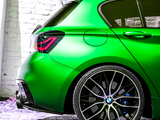 A vivid green car, positioned stationary, displays its rear wheel and taillight design against a white brick wall backdrop, emphasizing its sleek, sporty appearance.