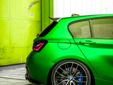Green sports car parked near a yellow and white wall. The image focuses on the rear wheel, which features a blue brake caliper and distinctive alloy design.