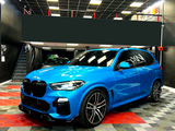 A blue BMW SUV is parked in a garage with a black ceiling and checkered red and black floor. 