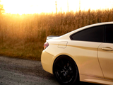 A yellow car is parked on a gravel road, with golden sunlight illuminating a field of tall grass in the background. The car's back wheel and tinted windows are visible.