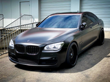 A sleek, matte black luxury sedan is parked on a paved surface. The vehicle is in front of a building with closed garage doors and a metal railing.