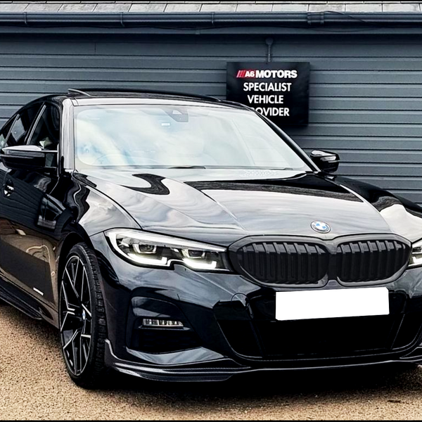 A sleek black car is parked on a pavement, positioned in front of a gray building. The sign reads “A6 Motors Specialist Vehicle Provider.”