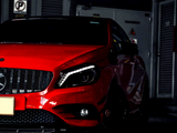 Red car parked in a dim garage, with its front prominently displayed against a dark background. A 
