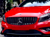 Red sports car with a prominent Mercedes-Benz logo on the grill, parked on a street lined with trees and buildings.