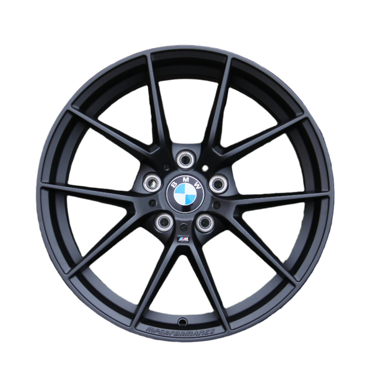A black BMW car wheel rim with a multi-spoke design showcases the BMW logo at the center. Text includes "BMW" and "M PERFORMANCE." The background is plain white.