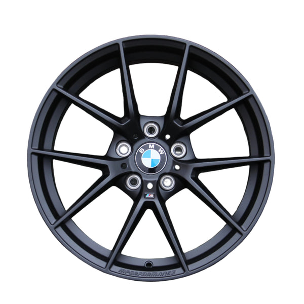 A black alloy wheel with a BMW logo at the center, featuring a multi-spoke design. Text includes "M PERFORMANCE" at the bottom edge and a small "M" badge. Background is white.