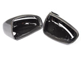 Two glossy black carbon fiber side mirror covers rest side by side, displaying their smooth, reflective surfaces against a plain white background.
