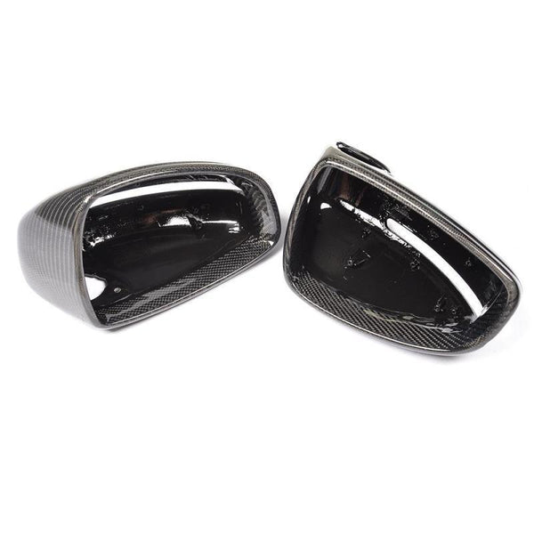 Two glossy black carbon fiber side mirror covers rest side by side, displaying their smooth, reflective surfaces against a plain white background.