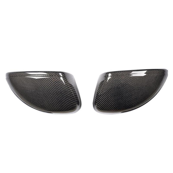 Two carbon fiber wing mirror covers are side by side, angled towards each other, against a plain white background. The covers have a glossy finish with a detailed woven pattern.
