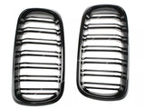 Two glossy black car grilles with horizontal slats are positioned side by side on a white background. Subtle reflections highlight their contours.