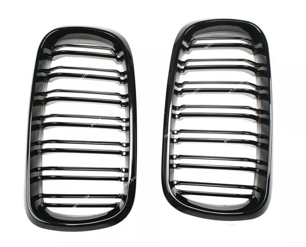 Two glossy black car grilles with horizontal slats are positioned side by side on a white background. Subtle reflections highlight their contours.