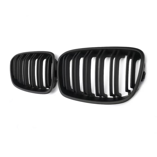 Black car grilles with vertical slats are positioned side by side, against a plain white background, emphasizing their design and structure.