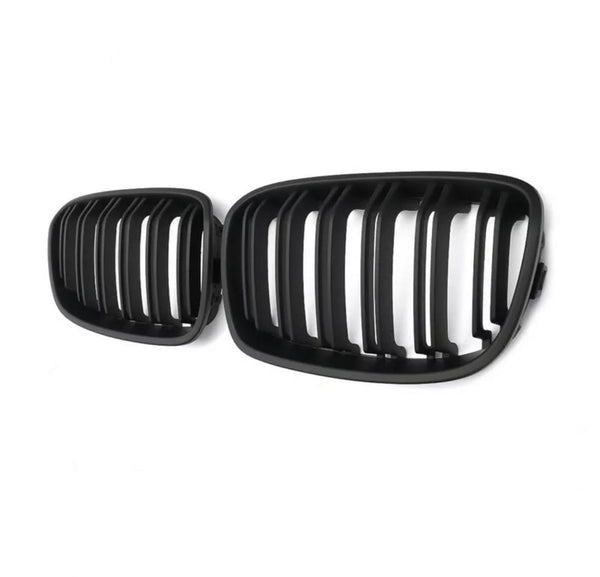 Black car grilles with vertical slats are positioned side by side, against a plain white background, emphasizing their design and structure.