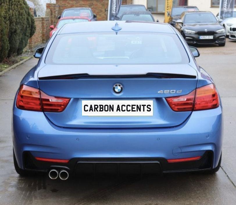A blue BMW 420d is parked outdoors on a concrete surface, featuring dual exhausts and red taillights. The rear license plate reads "CARBON ACCENTS." Numerous cars are visible in the background.