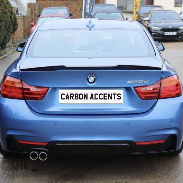 A blue BMW 420d is parked outdoors on a concrete surface, featuring dual exhausts and red taillights. The rear license plate reads "CARBON ACCENTS." Numerous cars are visible in the background.