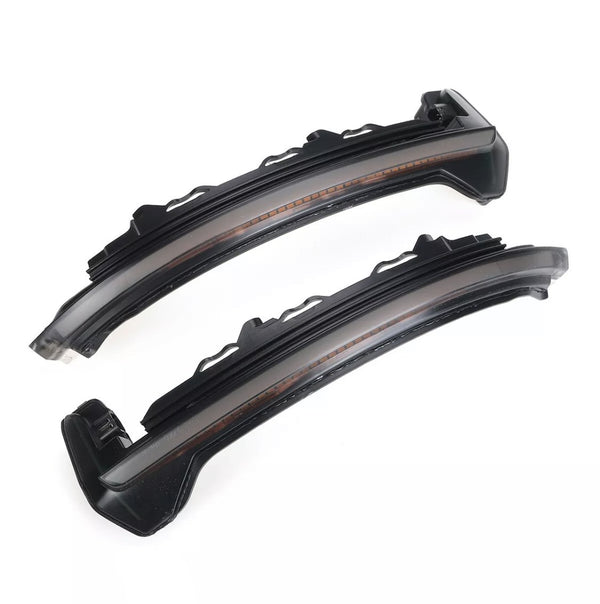 Two sleek black curved LED car lights with translucent covers lie side by side on a white background, showcasing their modern design intended for automotive use.