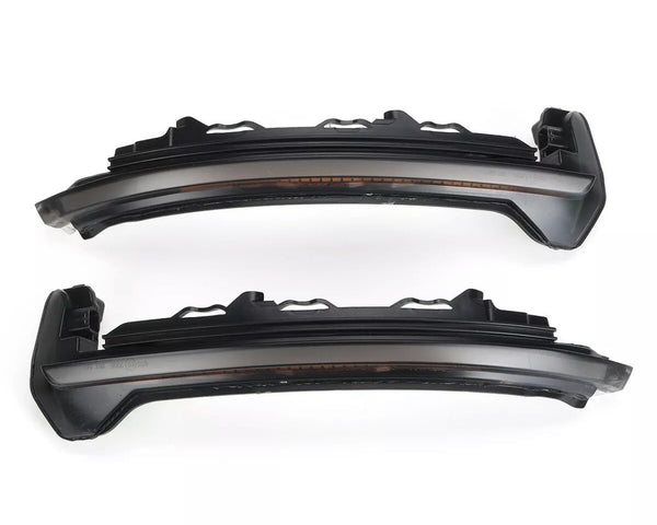 Two dark, curved car headlight components with intricate detailing are aligned horizontally on a plain white background, showing side profiles and a curved design for vehicle integration.