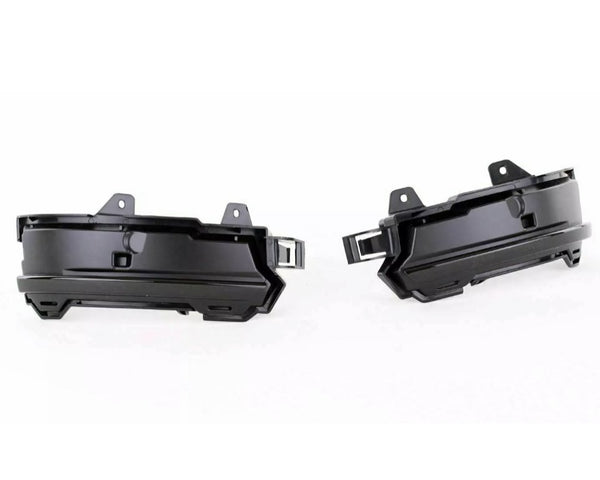 Two black plastic automotive parts, likely fog light housings, are positioned side by side facing outward. They feature mounting brackets and an angular design, set against a plain white background.
