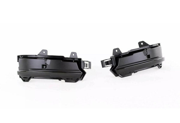 Two black plastic automotive parts, likely fog light housings, are positioned side by side facing outward. They feature mounting brackets and an angular design, set against a plain white background.