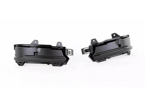 Two black plastic automotive parts, likely fog light housings, are positioned side by side facing outward. They feature mounting brackets and an angular design, set against a plain white background.