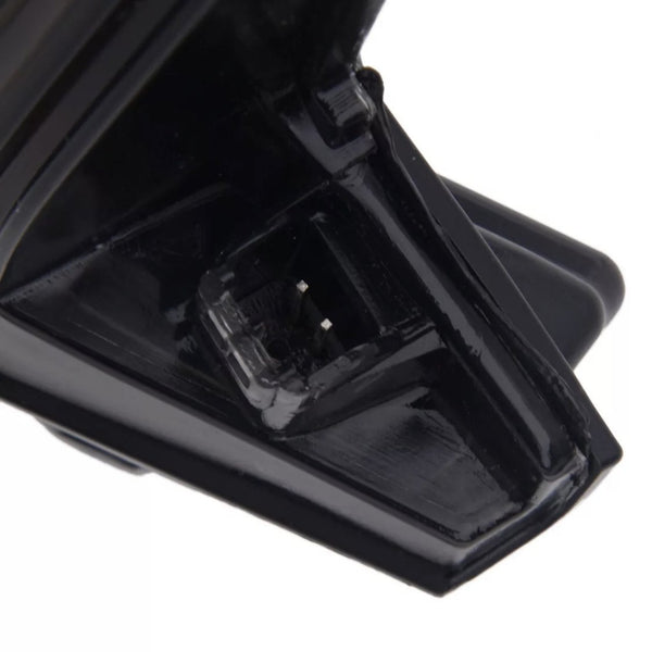 A black plastic part with a small square depression containing metal prongs, possibly for electrical connection, is shown against a plain background.