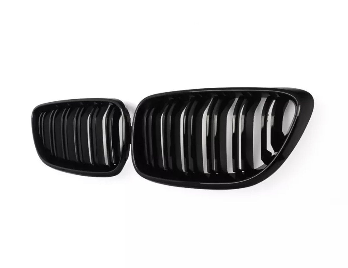 A pair of shiny, black car grilles with vertical slats are displayed against a plain white background, emphasizing their sleek, modern design.